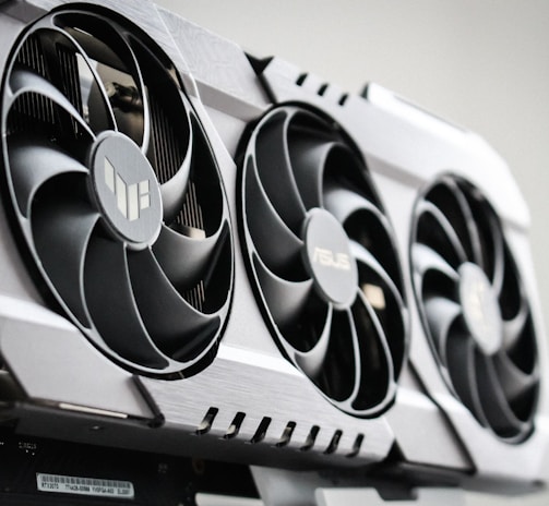 A close-up view of a graphics card with three large cooling fans and metallic accents. The card is housed within a computer case, showcasing intricate hardware design.
