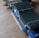 A computer graphics card rests on a wooden surface, showcasing intricate metallic heat sinks and a blue circuit board. The card features various electronic components and gold connectors for interfacing with a computer.