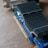 A computer graphics card rests on a wooden surface, showcasing intricate metallic heat sinks and a blue circuit board. The card features various electronic components and gold connectors for interfacing with a computer.