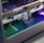 A close-up view of the interior of a computer casing showcasing a high-end graphics card with 'GeForce RTX' branding. The graphics card is secured in its slot, and several power cables are attached. The background reveals cooling fans illuminated with RGB lighting.
